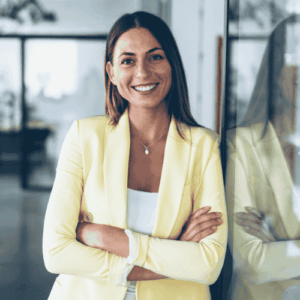 Professional woman in an office environment, smiling at the camera with arms crossed wearing a light yellow suit.