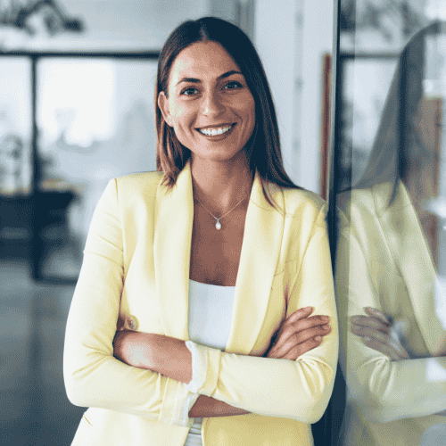 Professional woman in an office environment, smiling at the camera with arms crossed wearing a light yellow suit.
