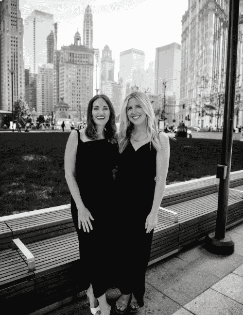 Black and white photo of matchmaker Erica Suzanne and Matchmaker Katie stood together wearing black in front of sky scrapers in downtown Chicago