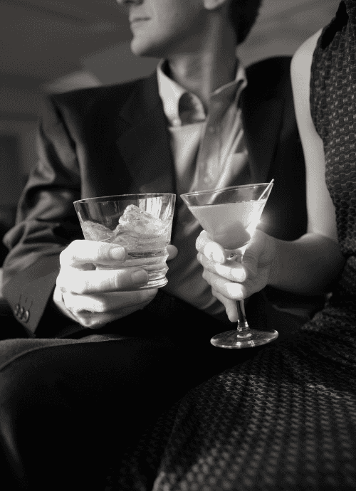 High class couple wearing suit with cocktails in their hands.