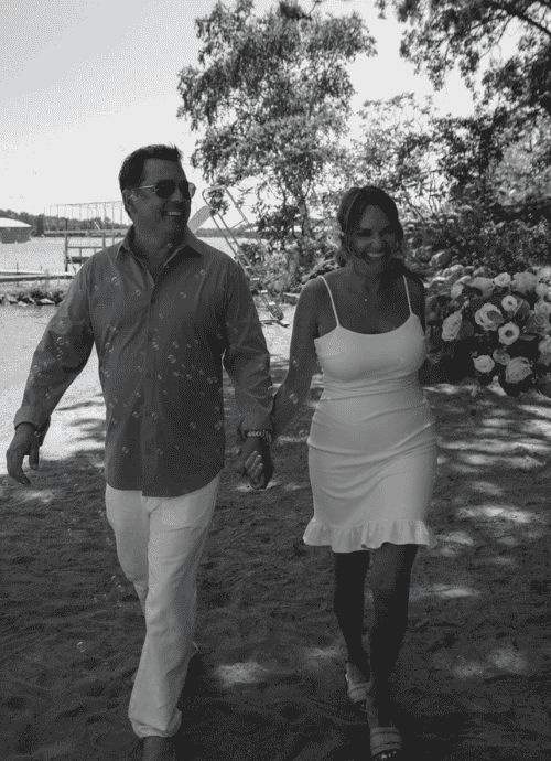 Black and white photo of Erica and Tom walking on a beach after getting married