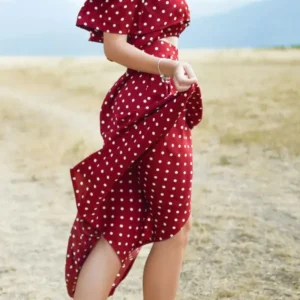 Image of a women wearing a red polka dot dress, slightly waving it in the wind with her left hand.